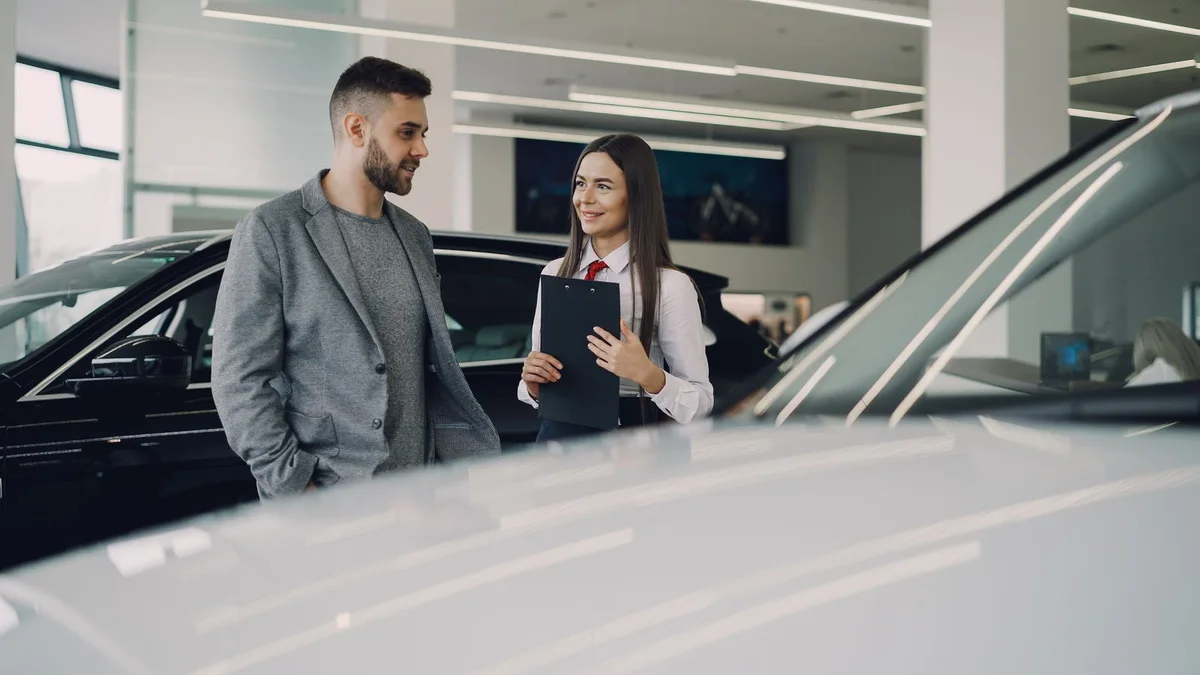 Acheter une voiture neuve : un acheteur face à une vendeuse dans un showroom de concession, au moment de la pire décision financière d'un budget