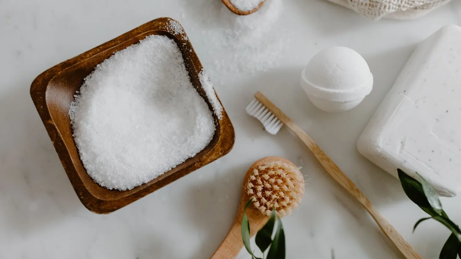 Bol en bois rempli de bicarbonate de soude entouré de brosses en bois, d'un savon et de feuillage pour un ménage naturel