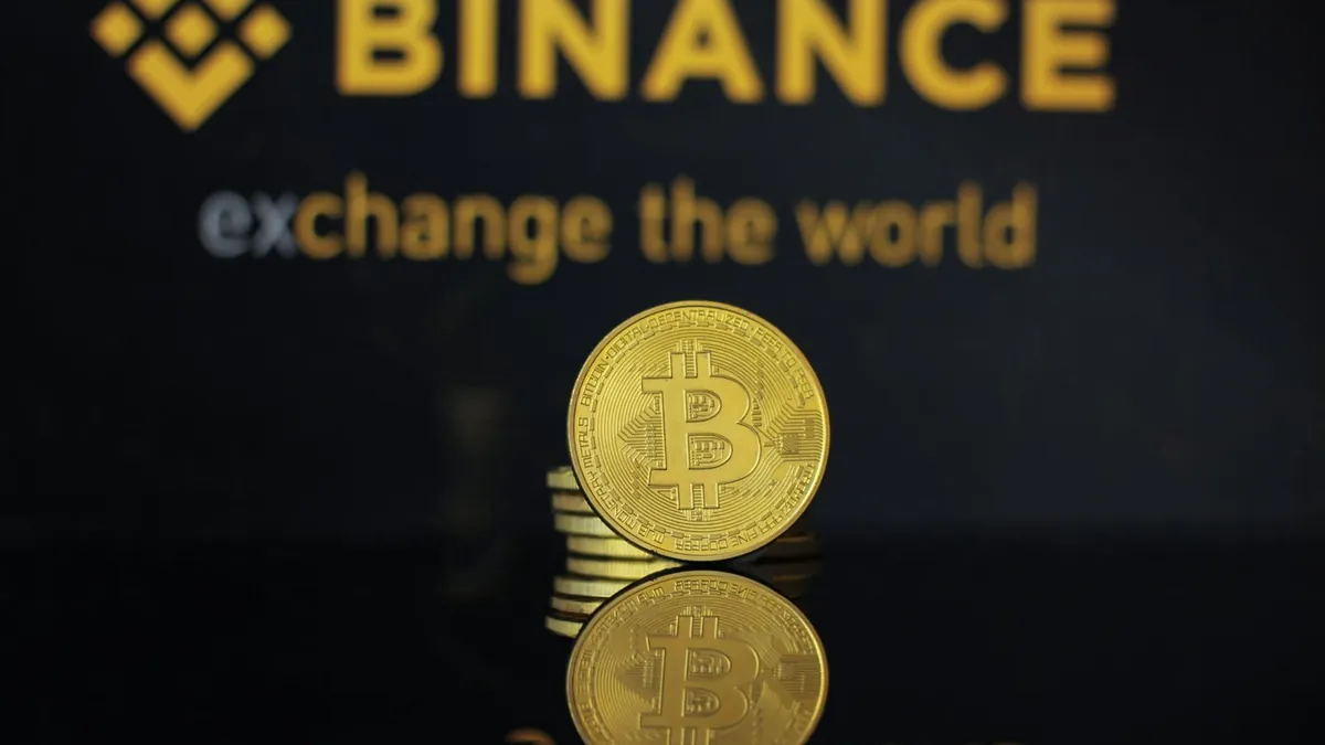 Logo Binance avec le slogan exchange the world et pièce Bitcoin dorée, illustrant l'arrêt des services crypto de Binance en France au 1er juillet 2026