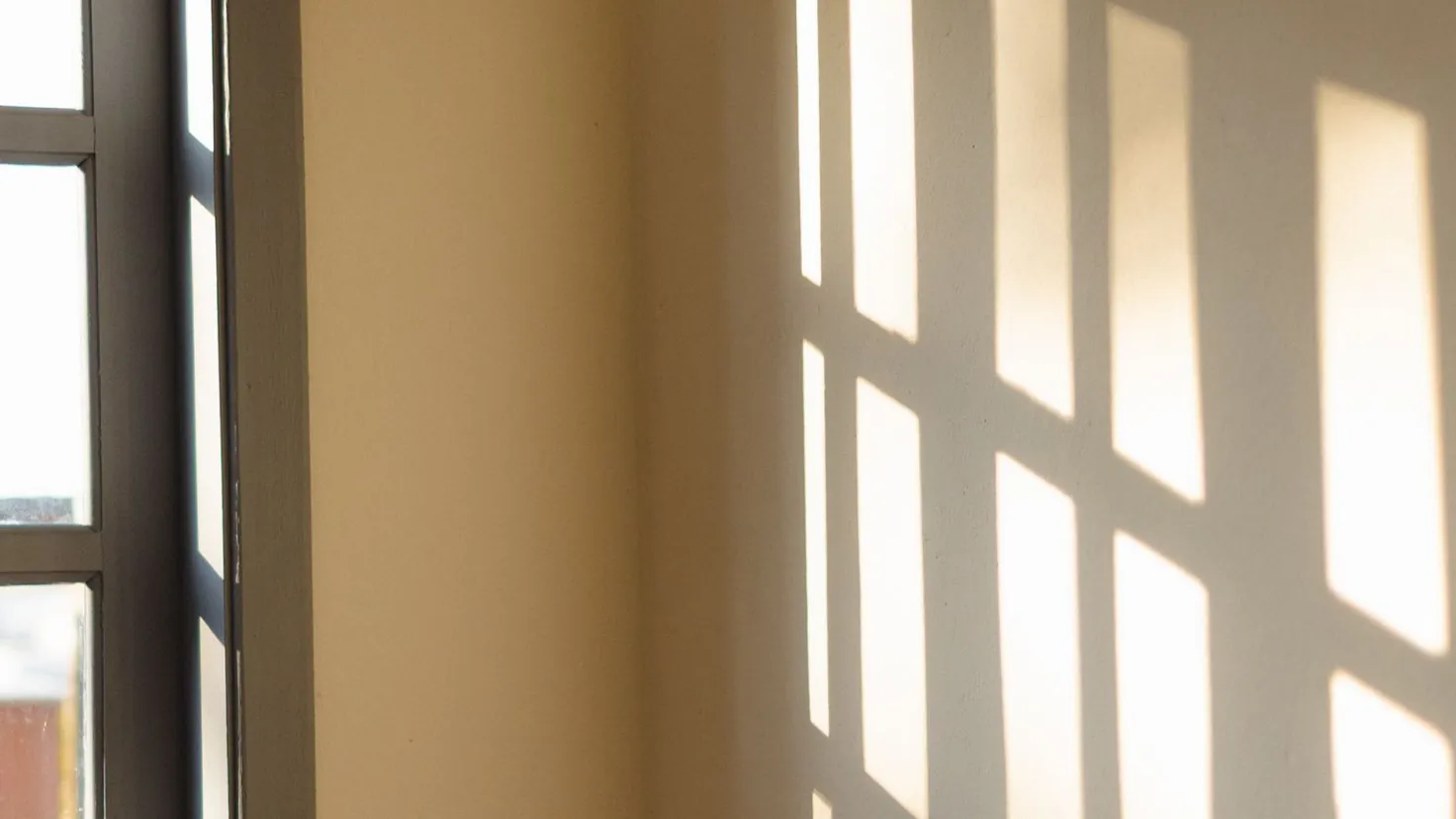 Soleil d'été tapant à travers une fenêtre et dessinant une grille de lumière chaude sur un mur intérieur