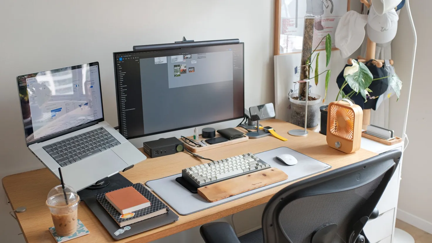 Poste de travail à domicile d'un entrepreneur menant son business à distance 2026 : ordinateur portable, écran externe avec éditeur de code, carnets et bureau en bois épuré