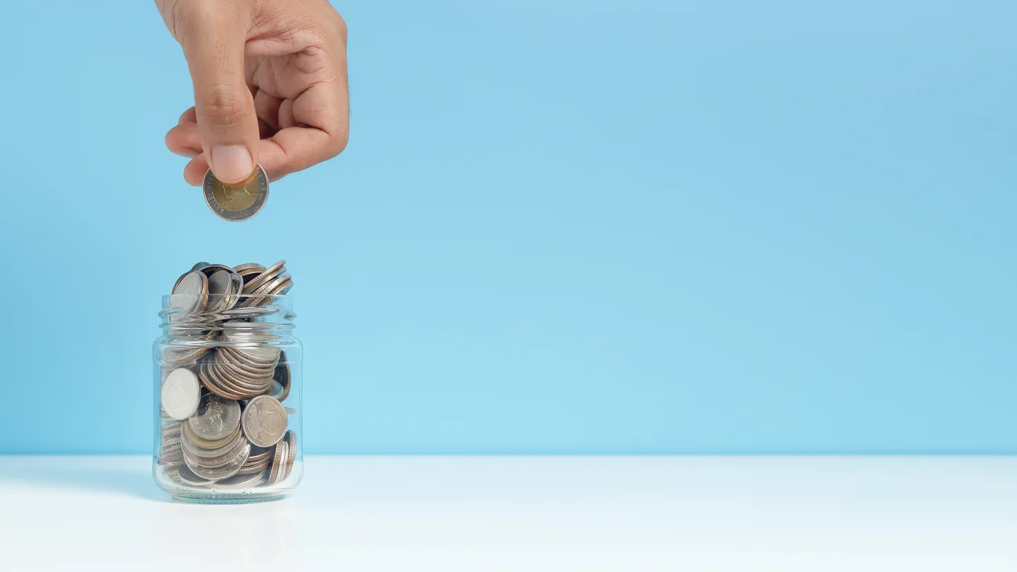 Comment investir régulièrement : une main dépose une pièce dans un bocal d'épargne, image du versement mensuel automatique