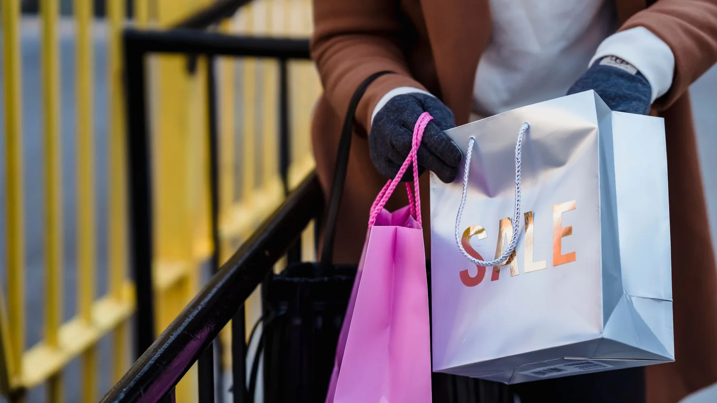 Achats impulsifs : une personne gantée tient deux sacs de shopping, dont un sac SALE de soldes, en haut d'un escalier
