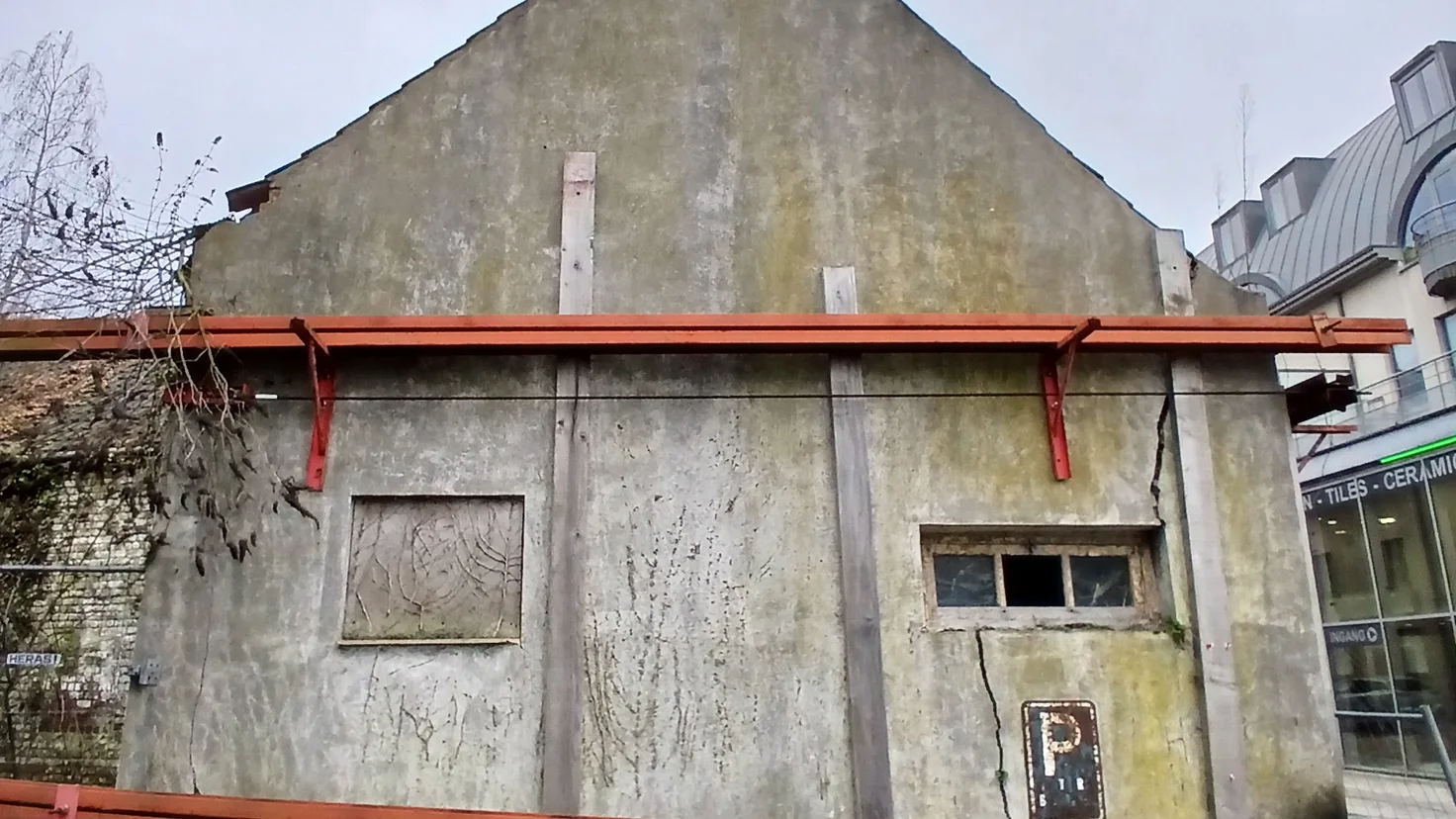 Pignon de maison présentant des fissures structurelles et un étaiement métallique de sécurité
