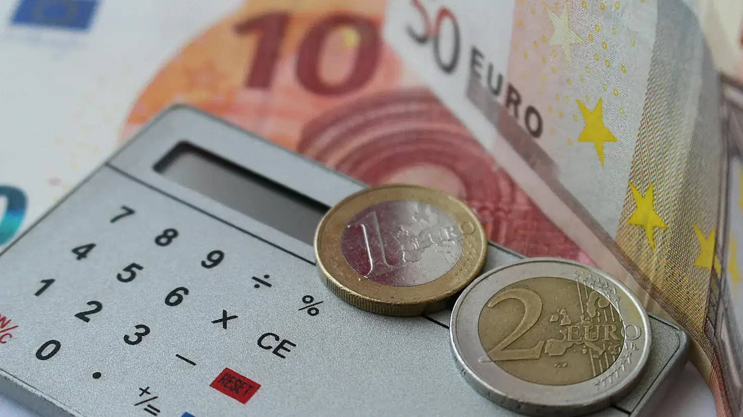 Calculatrice posée sur des billets et des pièces en euros, illustration de la flat tax et du PFU à 31,4 %