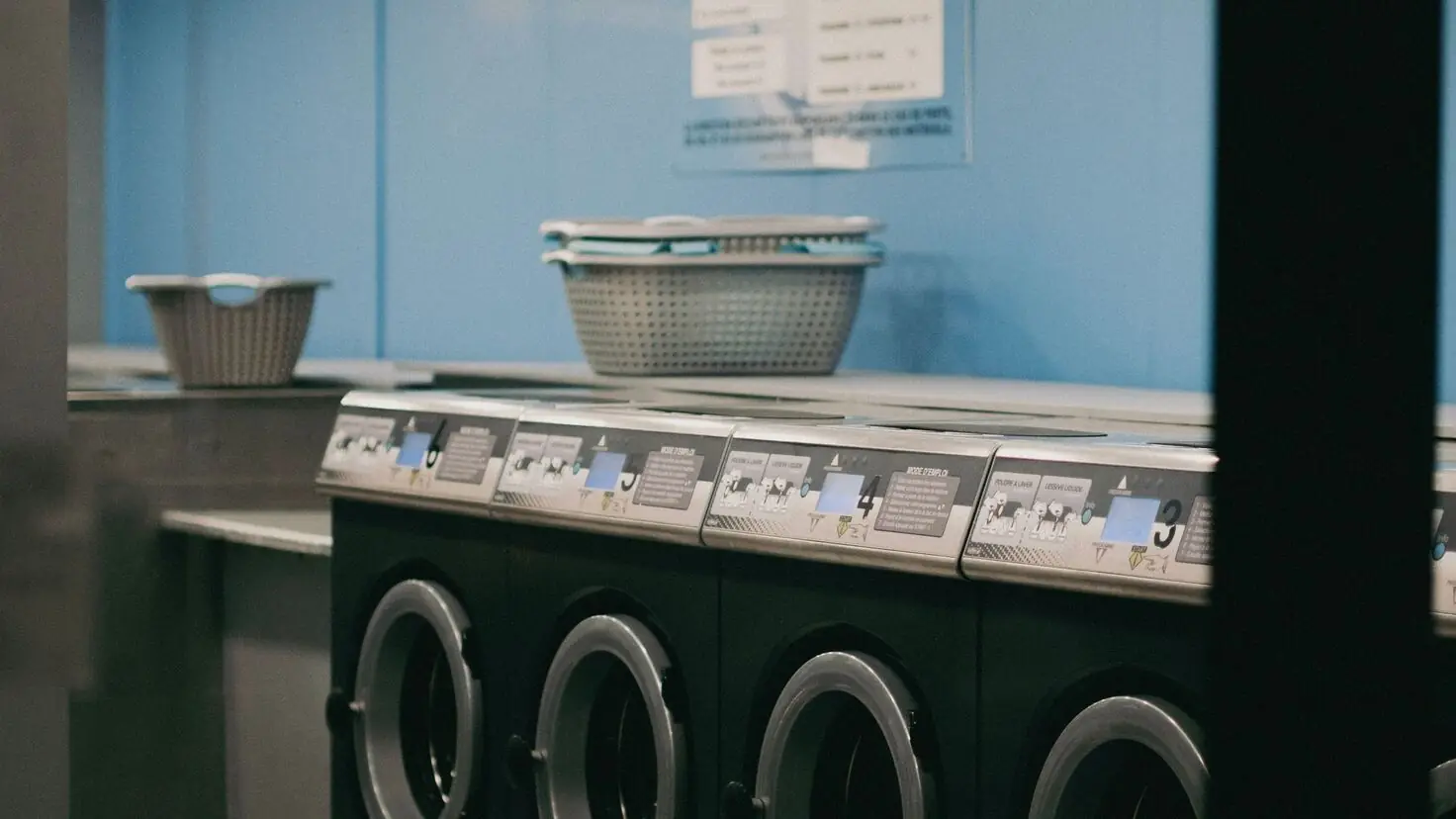 Intérieur d'une laverie automatique en libre-service avec une rangée de machines à laver frontales professionnelles numérotées et des paniers à linge, le cadre type pour investir dans une laverie automatique en 2026