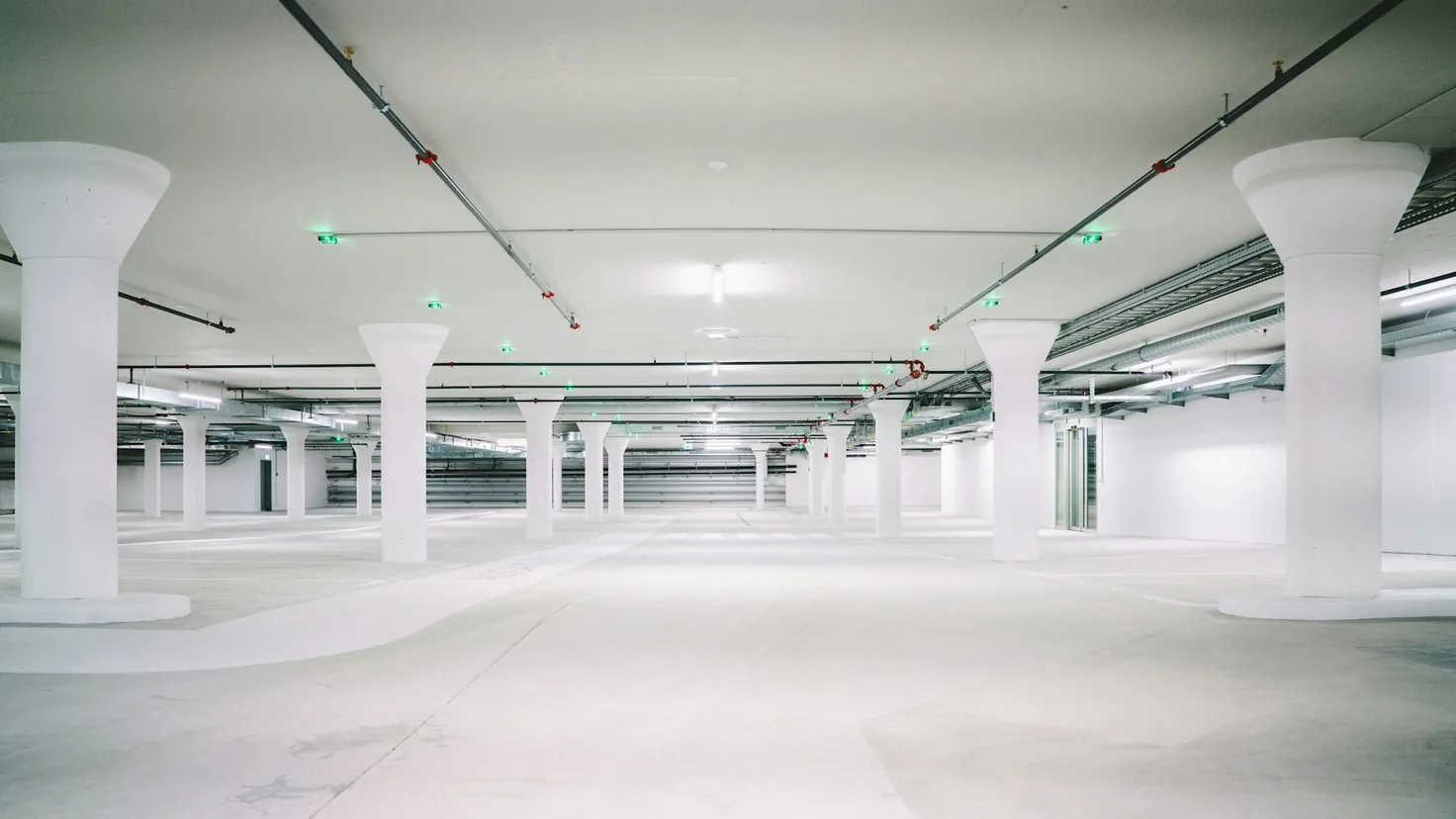 Investir parking en 2026 : parking souterrain vide aux piliers blancs et places marquées, illustration d'un investissement locatif en box et places de parking