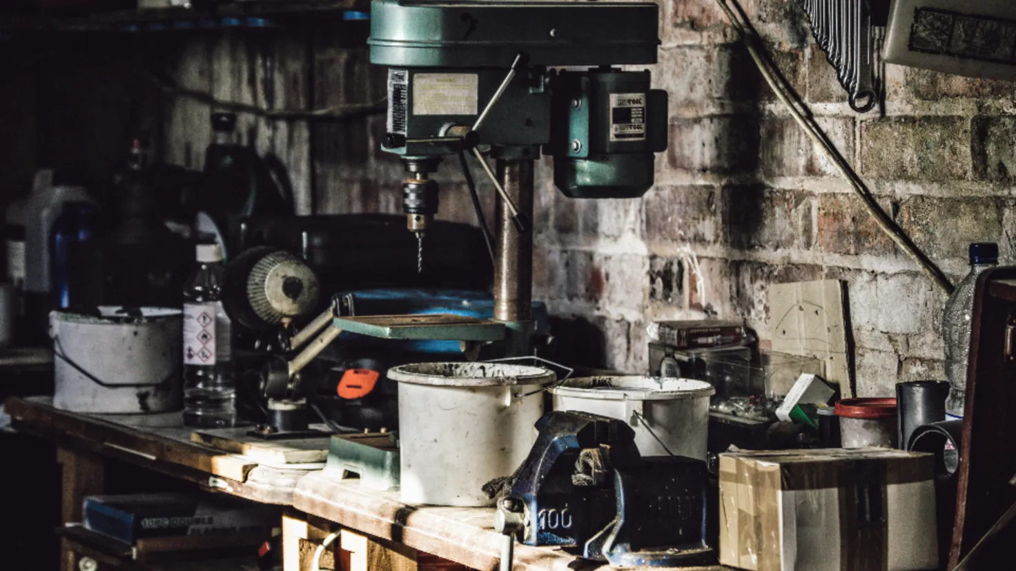 Perceuse à colonne et outils sur un établi encombré dans un atelier de garage, matériel type de la location entre particuliers