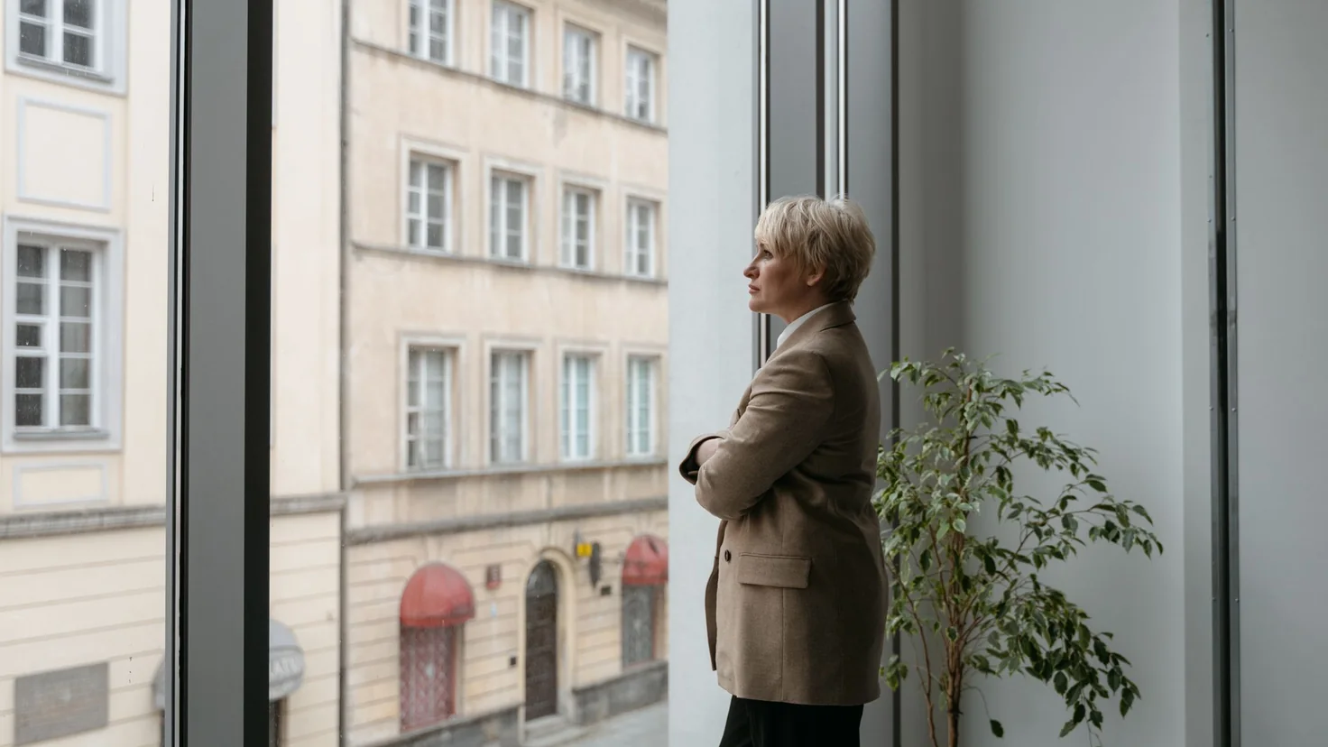 Salariée debout à la fenêtre d'un bureau, le regard tourné vers l'extérieur : l'image d'un travail vécu comme une prison dont on cherche à ne plus dépendre