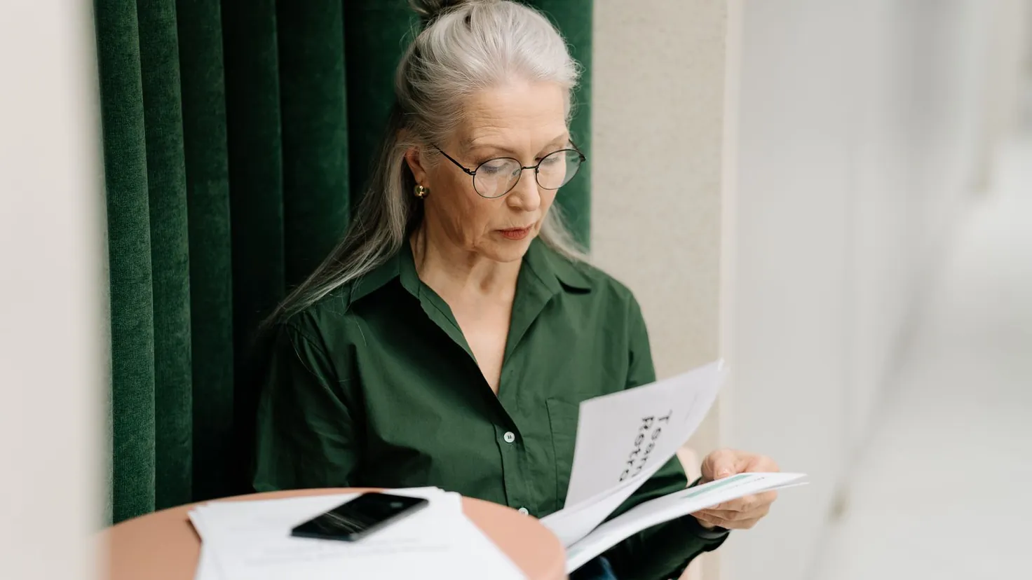Femme senior à lunettes consultant des documents administratifs liés à sa pension de réversion, lumière naturelle