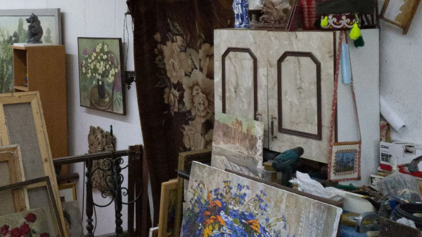 Tableaux encadrés empilés au sol devant une armoire et des bibelots dans une pièce à débarrasser après un décès