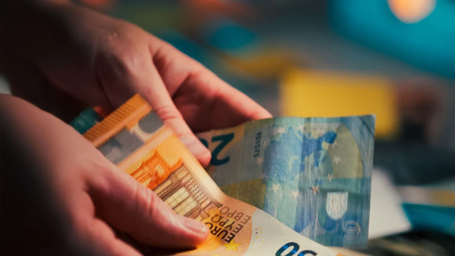 Mains qui comptent des billets de 20 et 50 euros au-dessus de billets en devise étrangère, illustration d’un budget serré pour vivre avec 800 euros par mois